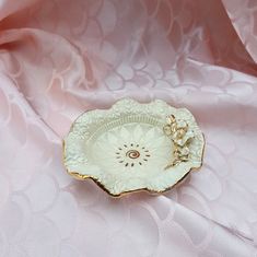 a white and gold plate sitting on top of a pink cloth covered table with a chain hanging from it's center