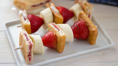 some strawberries and bananas are on a white plate with toothpicks in the shape of sandwiches