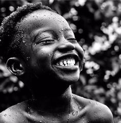 a black and white photo of a young boy laughing with water droplets on his face