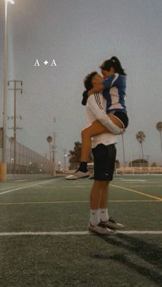 two people hugging each other on a tennis court with lights in the background and palm trees behind them