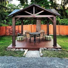 a wooden gazebo sitting on top of a lush green field next to a tree