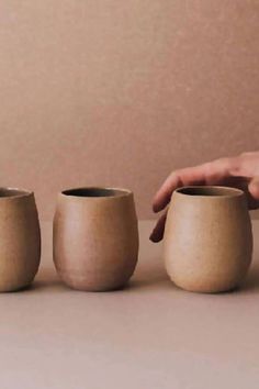 three handmade vases sitting on a table with one holding the other's thumb