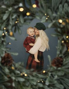 a woman holding a baby in front of a christmas wreath with lights on the background