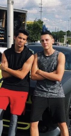 two young men standing next to each other in front of a car with their arms crossed