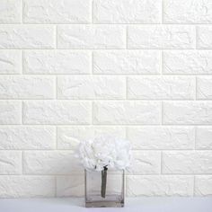 white flowers in a clear vase against a white brick wall