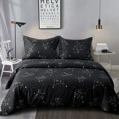 a bed with black comforter and pillows in a room next to a chair on the floor