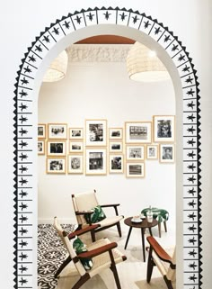 a room with chairs and pictures on the wall behind an arched doorway that leads to a sitting area