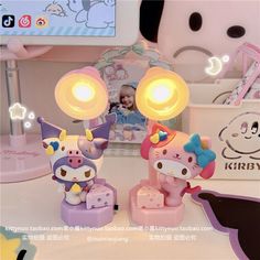 two hello kitty figurines sitting on top of a table next to a lamp