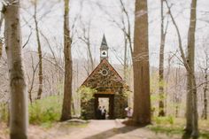 an old church in the woods with people walking through it and trees surrounding it,