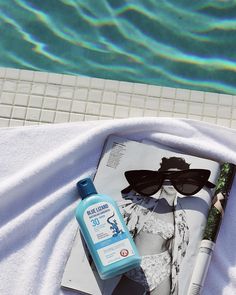 sunglasses and sunscreen on the edge of a swimming pool next to an open magazine