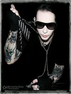 a man with tattoos and black sunglasses holding his arm up in the air while wearing a tie