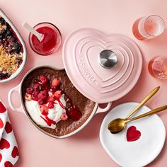 a heart - shaped dish with strawberries and other desserts next to it on a pink surface