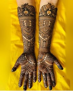 two hands with henna designs on them and yellow sheets in the backgroud