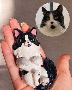 a black and white cat figurine sitting on top of a persons hand next to a photo