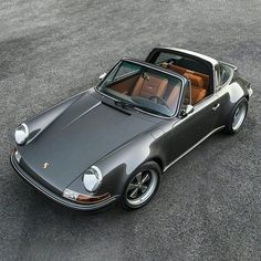 a gray porsche sits parked in a parking lot with its top down and the roof down