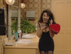 a woman holding a red heart while standing in front of a bathroom mirror and talking on the phone