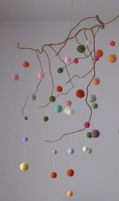 a mobile made out of felt balls hanging from a tree branch in a white room