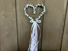 a heart shaped wreath with white flowers hanging on a wooden wall next to a fence