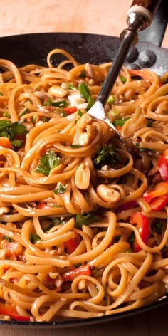 a pan filled with noodles and vegetables on top of a wooden table next to a fork