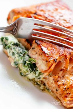 a piece of salmon with spinach and cheese on it being held by a fork