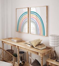 a wooden table topped with books next to two framed rainbows on the wall above it