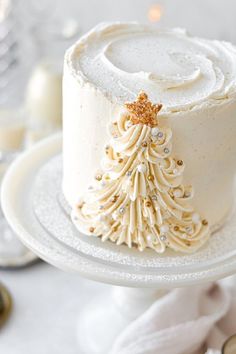 a white frosted cake decorated with a gold christmas tree on top and some candles in the background