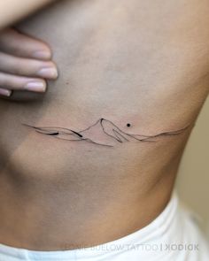 a woman's stomach with a small mountain tattoo on her left side ribcage