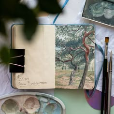 an artist's notebook with watercolors and paintbrushes on the table