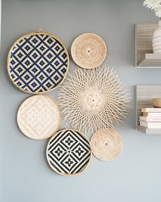 four woven baskets are hanging on the wall next to two books and a vase with flowers