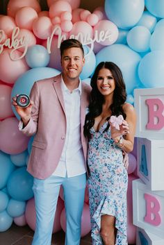 a man and woman standing next to each other in front of balloons with baby names on them