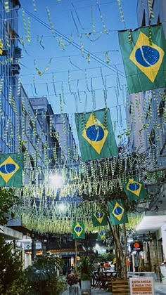 many flags are hanging in the air near some trees and buildings with lights on them