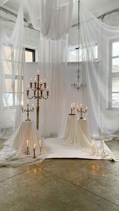 a room with white curtains and candles on the floor in front of it is a chandelier