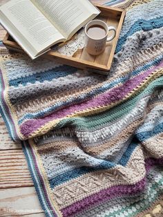 an open book and cup of coffee on top of a multicolored crocheted blanket