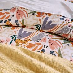 an unmade bed with yellow sheets and floral print on it, next to a white comforter