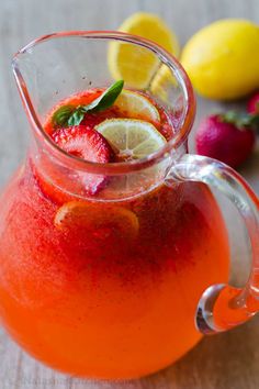 a pitcher filled with fruit and garnish on top of a wooden table next to lemons