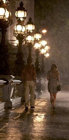 two people walking down the street in the rain with their umbrellas open and lights on