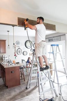 a man standing on top of a ladder while holding a drill and hammer in his hand