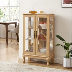 a wooden cabinet with glass doors and shelves in a living room next to a potted plant