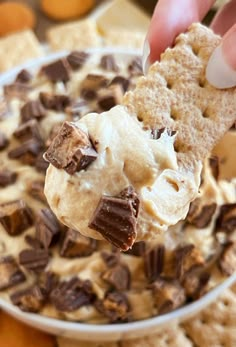 a hand holding a cracker over a bowl of dip with chocolate chips on top