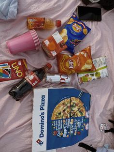 the contents of a pizza and snacks laid out on a pink sheeted bed spread