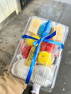 a person holding a plastic container filled with different types of candies and fruit in it