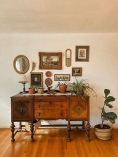 a wooden table topped with potted plants next to a wall filled with framed pictures