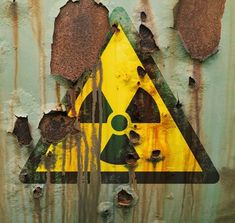 a yellow and black hazard sign on the side of a rusted metal wall with peeling paint