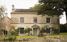 an old stone house with ivy growing all over it's walls and windows, along with a bench in the front yard