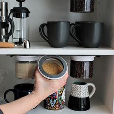 a person holding a coffee cup in front of some coffee mugs on a shelf