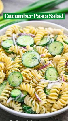 a bowl filled with pasta and cucumbers on top of a table next to green onions