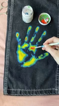 someone is painting their hand on a black piece of cloth with yellow and blue paint