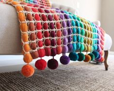 a multicolored crocheted pillow with pom - poms hanging from it