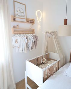 a baby's crib in the corner of a room with clothes hanging up