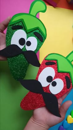 two handmade chili pepper puppets are being held up by someone's hands with green and red sequins on them